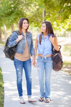 Two Beautiful Young Ethnic Twin Sisters With Backpacks Walking Outdoors.