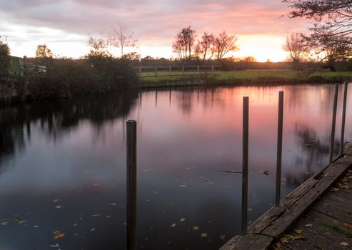 beautiful long exposure of red autumn blurred water lake river surface dock side wooden posts; essex; england; uk