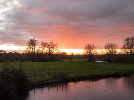red sun setting sky dramatic autumn over empty open green countryside night dark lake; essex; england; uk