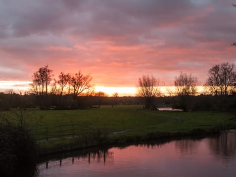 red sun setting sky dramatic autumn over empty open green countryside night dark lake; essex; england; uk