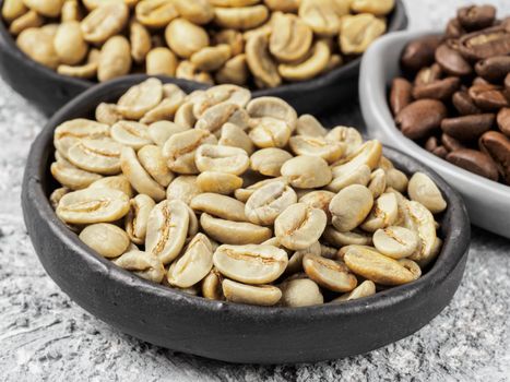 Close up view of raw green coffee beans in trendy plate on gray concrete background. White and brown coffee on background. Image with natural colors