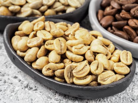 Close up view of raw white coffee beans in trendy plate on gray concrete background. Green and brown coffee on background. Image with natural colors