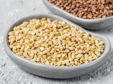 Close up view of raw green buckwheat in trendy plate and brown roasted buckwheat on background. Healthy food and diet concept