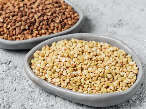 Close up view of raw green buckwheat in trendy plate and brown roasted buckwheat on background. Healthy food and diet concept