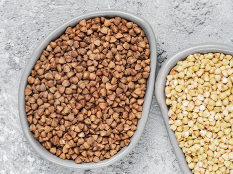 Top view of brown roasted buckwheat and raw green buckwheat in trendy plates on gray concrete background. Healthy food and diet concept. Flat lay. Copy space.