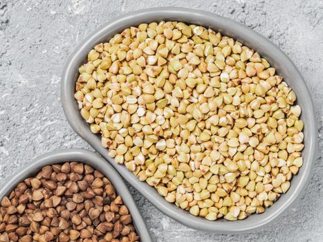 Close up view of raw green buckwheat in trandy plate and brown roasted buckwheat on background. Healthy food and diet concept. Top view or flat lay