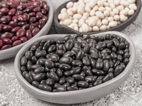 Close up view of raw black beans in trendy plate on gray concrete background. Red and white beans on background.