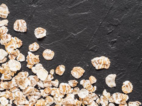 Dry oatmeal on black concrete background with copy space. Raw oatmeal texture. Top view or flat lay