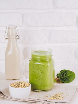 Close up view of green smoothie in mason jar on white table. Fresh green smoothie with green buckwheat, spinach and vegan milk. Copy space. Vertical.