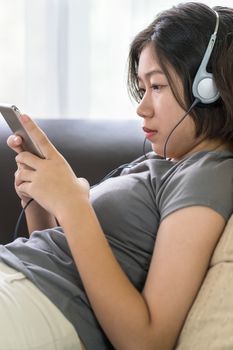 Close up young asian woman short hair listening music from mobile phone on the couch at home