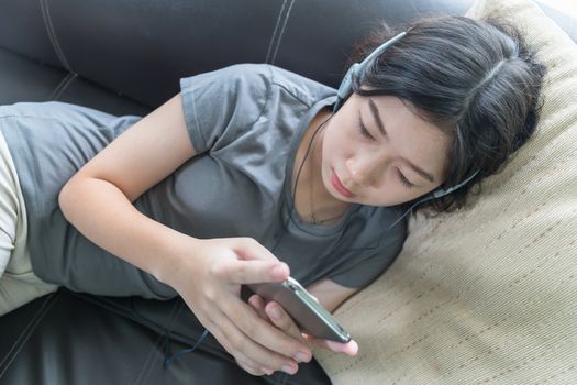 Close up young asian woman short hair listening music from mobile phone on the couch at home