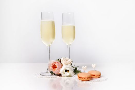 Two glasses with champagne, boutonniere with roses and cookies