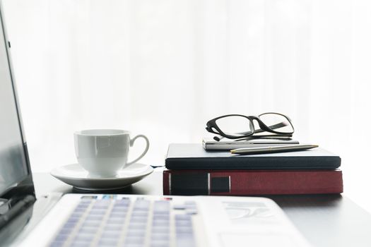 Close up laptop placed on desktop with coffee cup and glasses on book in room at home office