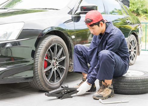 Young mechanic in uniform replacing lug nuts by hand while changing tires on a vehicle
