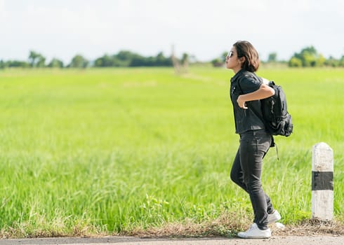 Young asian woman short hair and wearing sunglasses with backpack hitchhiking along a road in countryside Thailand