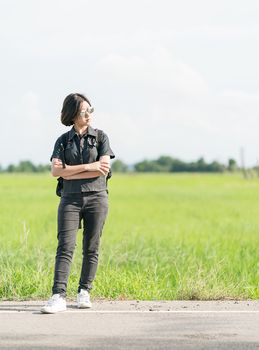 Young asian woman short hair and wearing sunglasses with backpack hitchhiking along a road in countryside Thailand