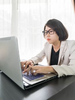 Woman short hair in smart casual wear working on laptop while sitting near window in home office