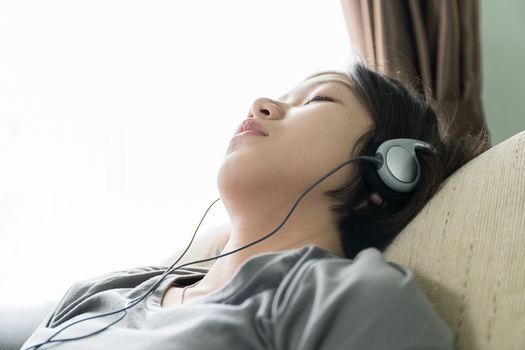 Close up beautiful young asian woman short hair listening music on the couch at home