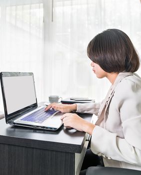 Young asian woman short hair in smart casual wear working on laptop while sitting near window in home office