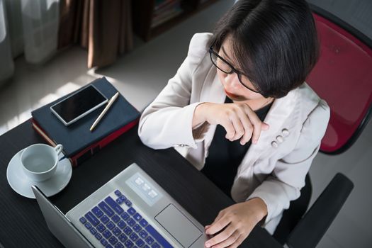 Young asian woman short hair in smart casual wear working on laptop while sitting near window in home office