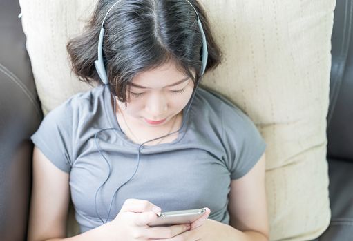 Close up young asian woman short hair listening music from mobile phone on the couch