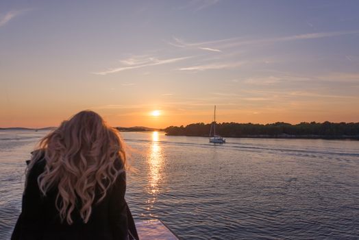 Woman traveling by boat at sunset among the islands, sailing boats and yachts in background