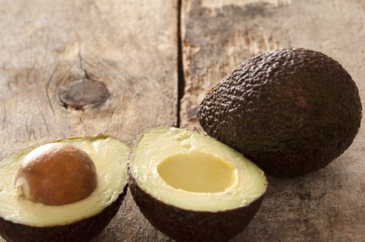 Tasty whole and halved ripe avocado pears with the pip still in forming a border with copy space on rustic wood