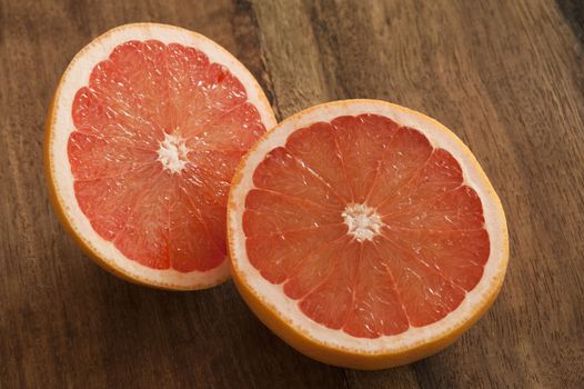 Fresh cut pink grapefruit halves showing the juicy acidic pulp and segments on a wooden kitchen table ready to be served for breakfast