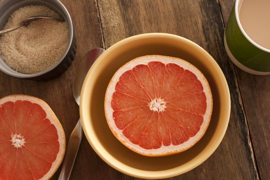 Halved fresh pink or rose grapefruit served in a bowl for breakfast with an accompanying basin of caramelized sugar, overhead view