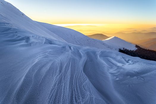 Winter evening in the Ukrainian Carpathians. Gentle sun rays enlighten snowy mountain ridge. Traces of wind and frost in the snow. Mountains on the background is blurred.