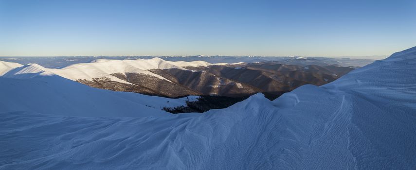 Winter in the Ukrainian Carpathians. Snowy mountain ridge. Traces of wind and frost in the snow. Wide panorama