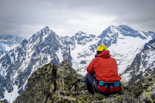 A climber looking at the snow-capped mountains sitting on a rock. High Tatras, Slovakia