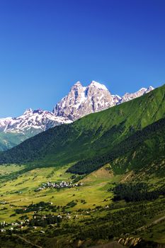 Ushba mountain on the background of a clean blue sky. In the valley there are small villages. Summer in Georgia. Svaneti.