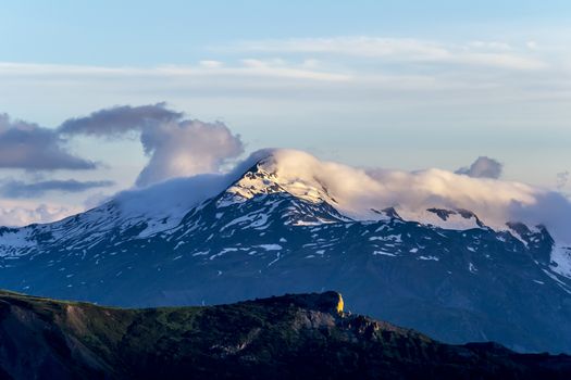 Mountain landscape. Peak with snow in evening sunlight and a cloud above. Summer in Georgia.