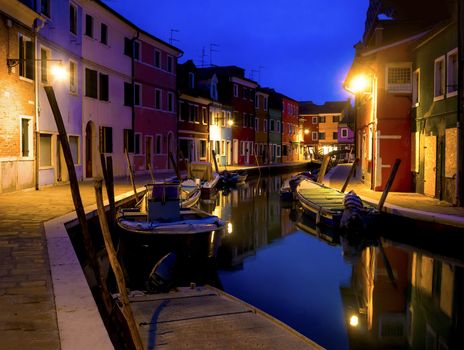 Quiet evening cityscape of Burano island in Venice. Colored buildings are illuminated by street lights on the background of the water channel and the small bridge.