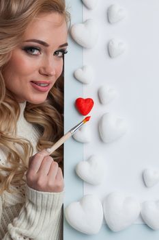 Young happy woman painting in red decorative hearts, Valentines day concept