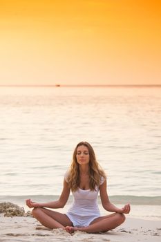 Young woman practicing yoga on the beach at sunset