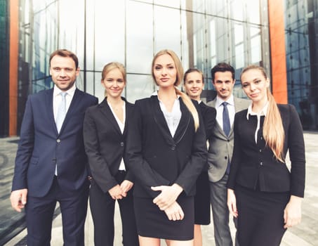 Portrait of successful business people team standing together outdoors near modern office building