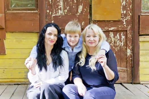 Three people two women and teenager boy are sitting at wooden porch