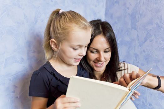 Cute smiling daughter are reading a book with her mother