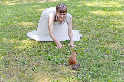 Bride in white lying on green grass next to the squirrel in summer