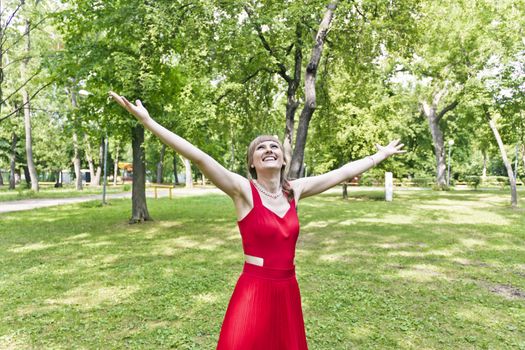 Beautiful lady in red are standing at summer day with upward hands