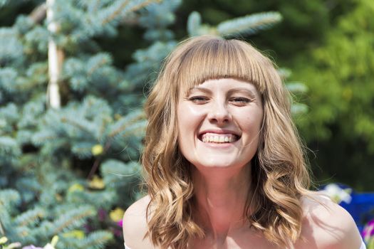 Portrait of laughing young woman with blond hair on summer background