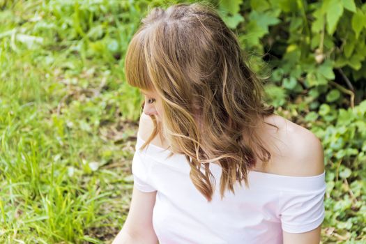 Young woman with blond hair sitting on green grass in summer