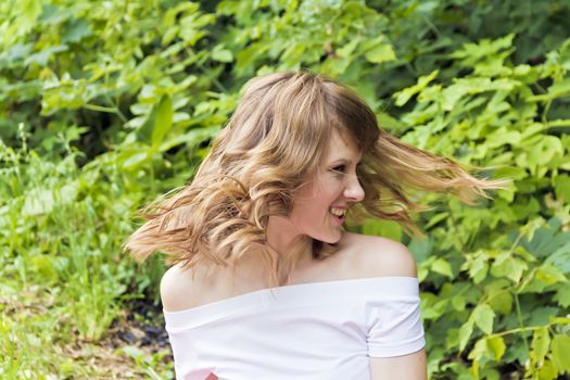 Young woman are playing with own blond hair on summer background