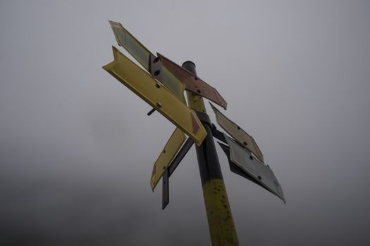A pole with several, five usable, empty mountain road direction pointers in cold misty weather.