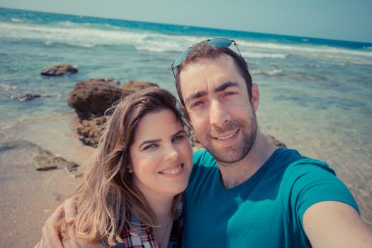 Young couple taking selfie with smartphone or camera at the beach.