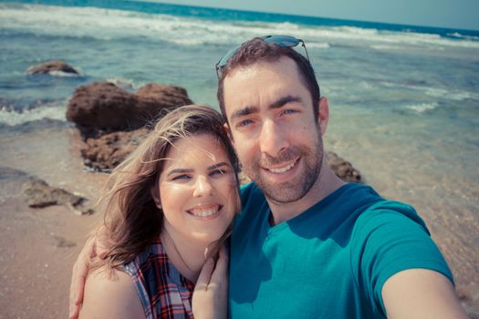 Young couple taking selfie with smartphone or camera at the beach.