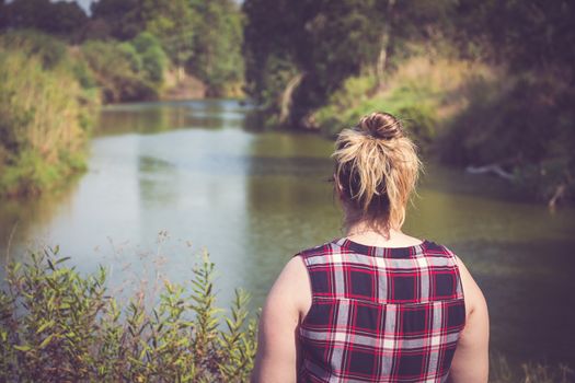 Back view of woman standing and looking away at banks of the river. Relaxation and meditation concept.