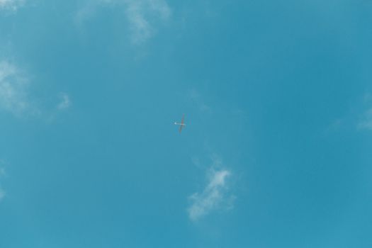 Glider gliding in blue sky from below.